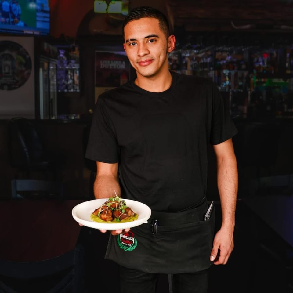 A Potrillo's Mexican Grill server holds a plate of Mexican food with a green sauce.