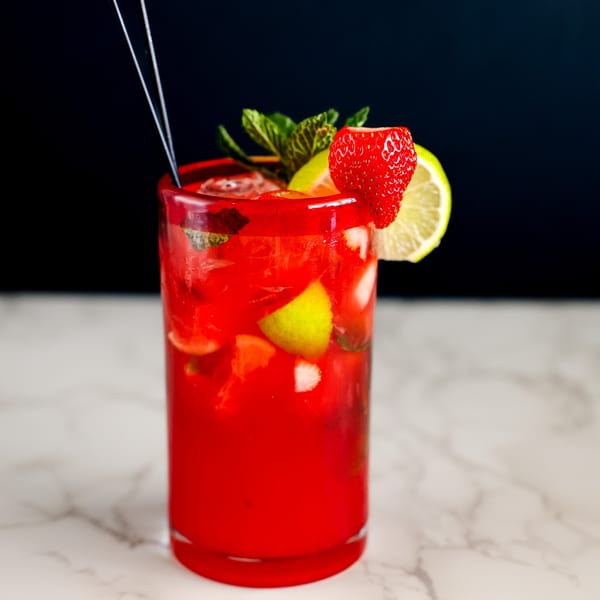 A vibrant red strawberry mojito with lime, mint, and ice, garnished with a strawberry and lime slice.