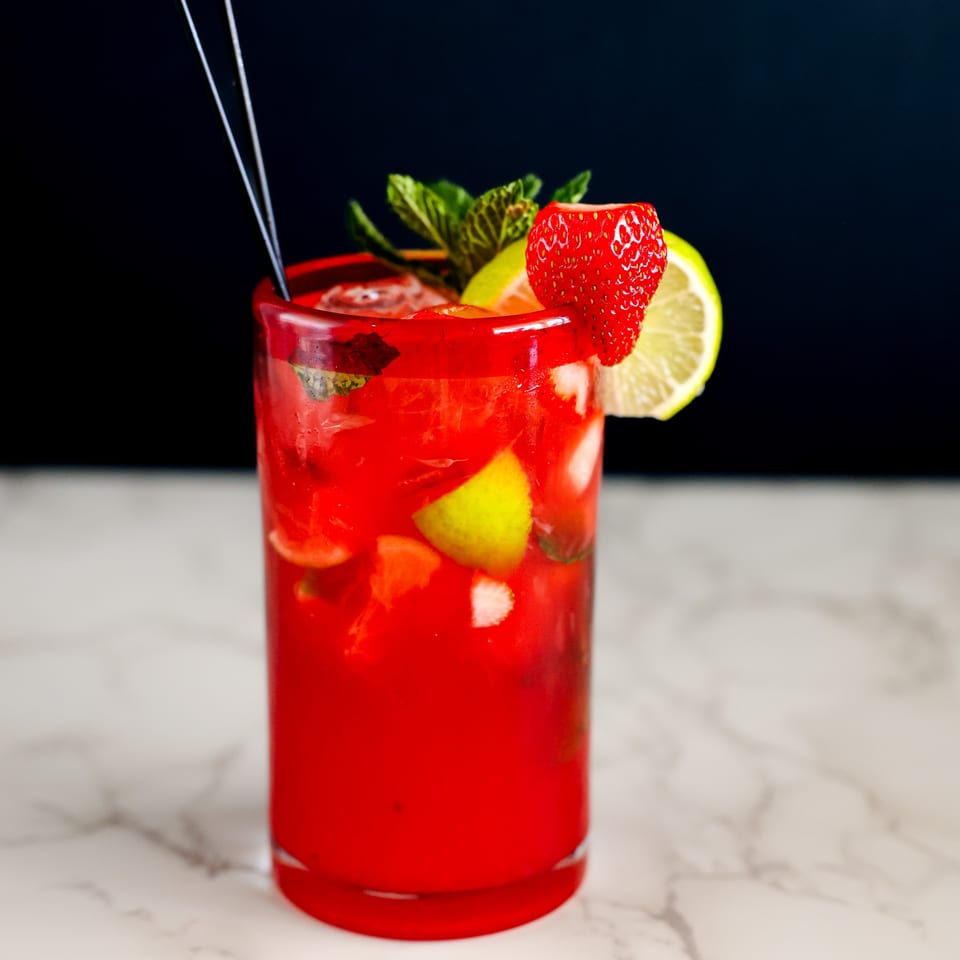 A vibrant red strawberry mojito with lime, mint, and ice, garnished with a strawberry and lime slice.