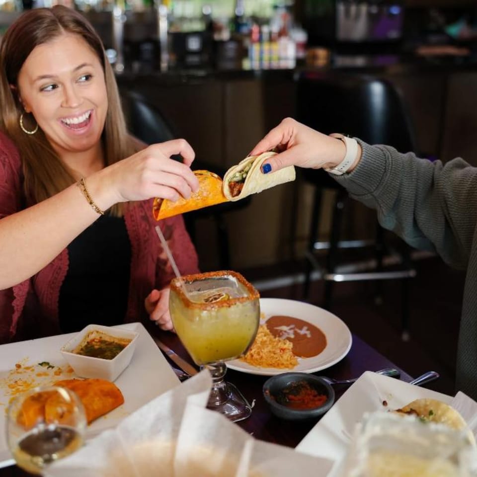 Two people sharing tacos and drinks at Potrillo's Mexican Grill, with plates of food on the table.