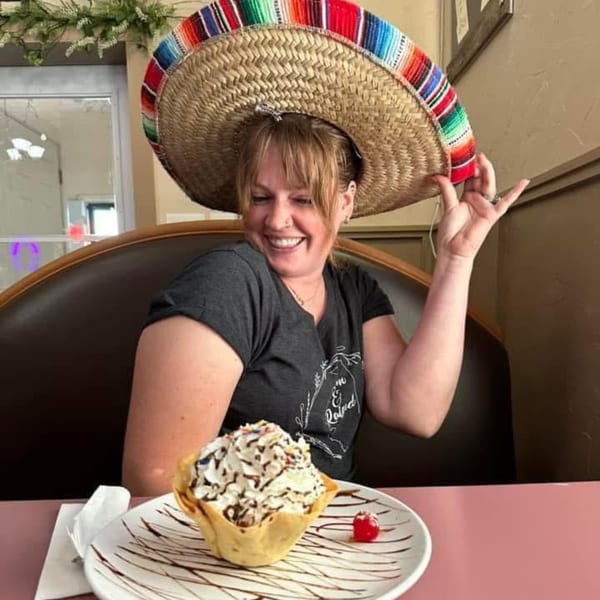 A smiling woman wearing a sombrero, with a dessert in a tortilla bowl in front of her.