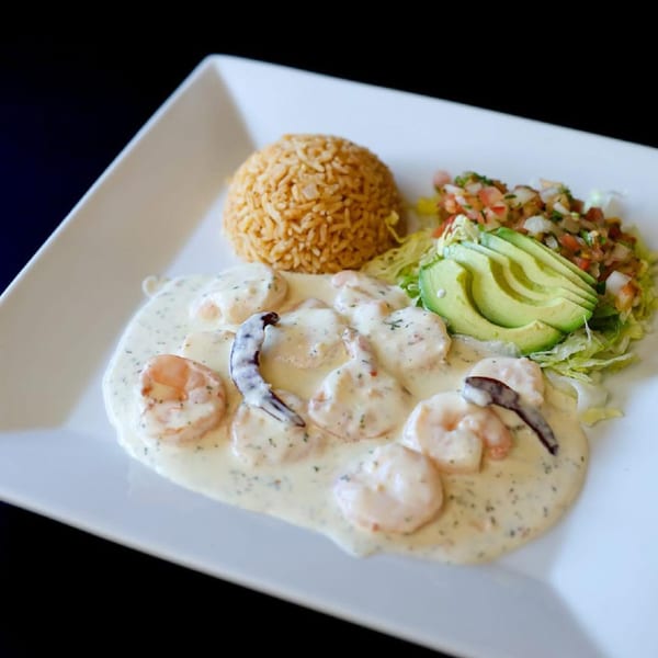 Shrimp in a creamy sauce with rice, avocado, and pico de gallo on a white plate.
