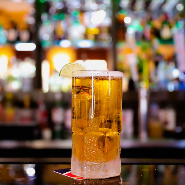 A tall, frosty glass of golden Mexican beer with a lime wedge on a bar top.