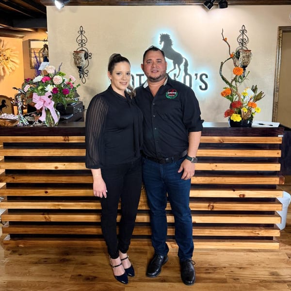 A man and woman stand in front of a Potrillo's Mexican Grill sign with a horse logo.
