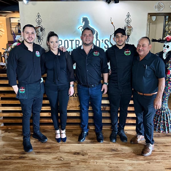 Five Potrillo's Mexican Grill staff members in black uniforms stand smiling in front of a neon sign.