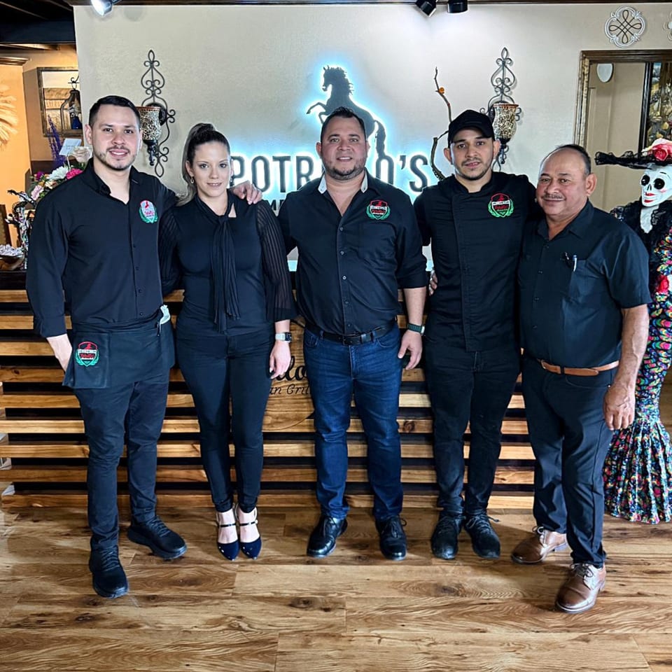 Five Potrillo's Mexican Grill staff members in black uniforms stand smiling in front of a neon sign.