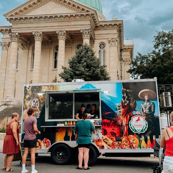Potrillo's Mexican Grill food truck with customers, parked in front of a large stone building.
