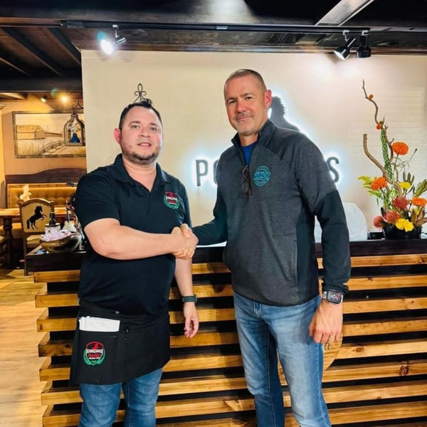 Two men shaking hands in front of the Potrillo's Mexican Grill reception desk with a floral arrangement.