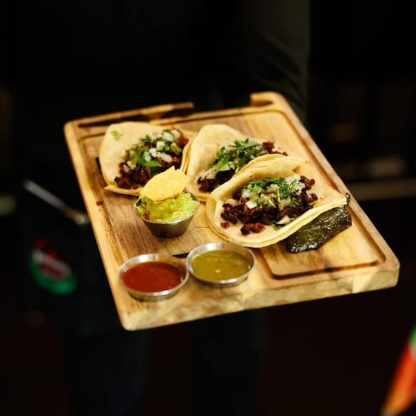 Three Potrillo's Mexican Grill tacos with guacamole and two salsas on a wooden board.