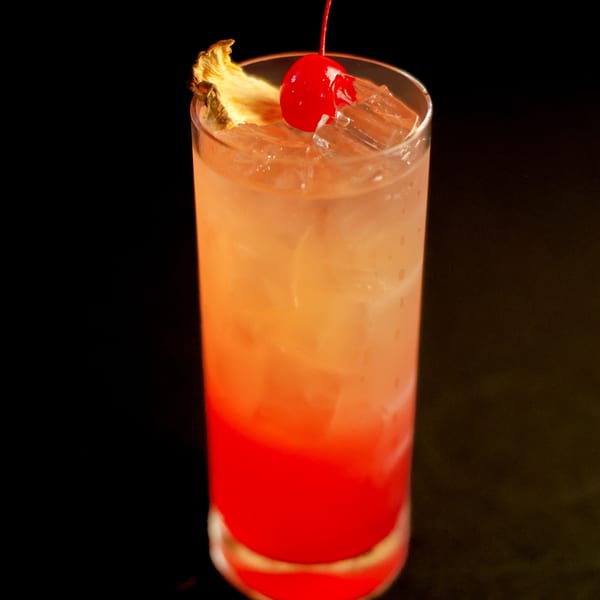 Potrillo's Mexican Grill's vibrant red and orange cocktail, garnished with a pineapple slice and cherry.