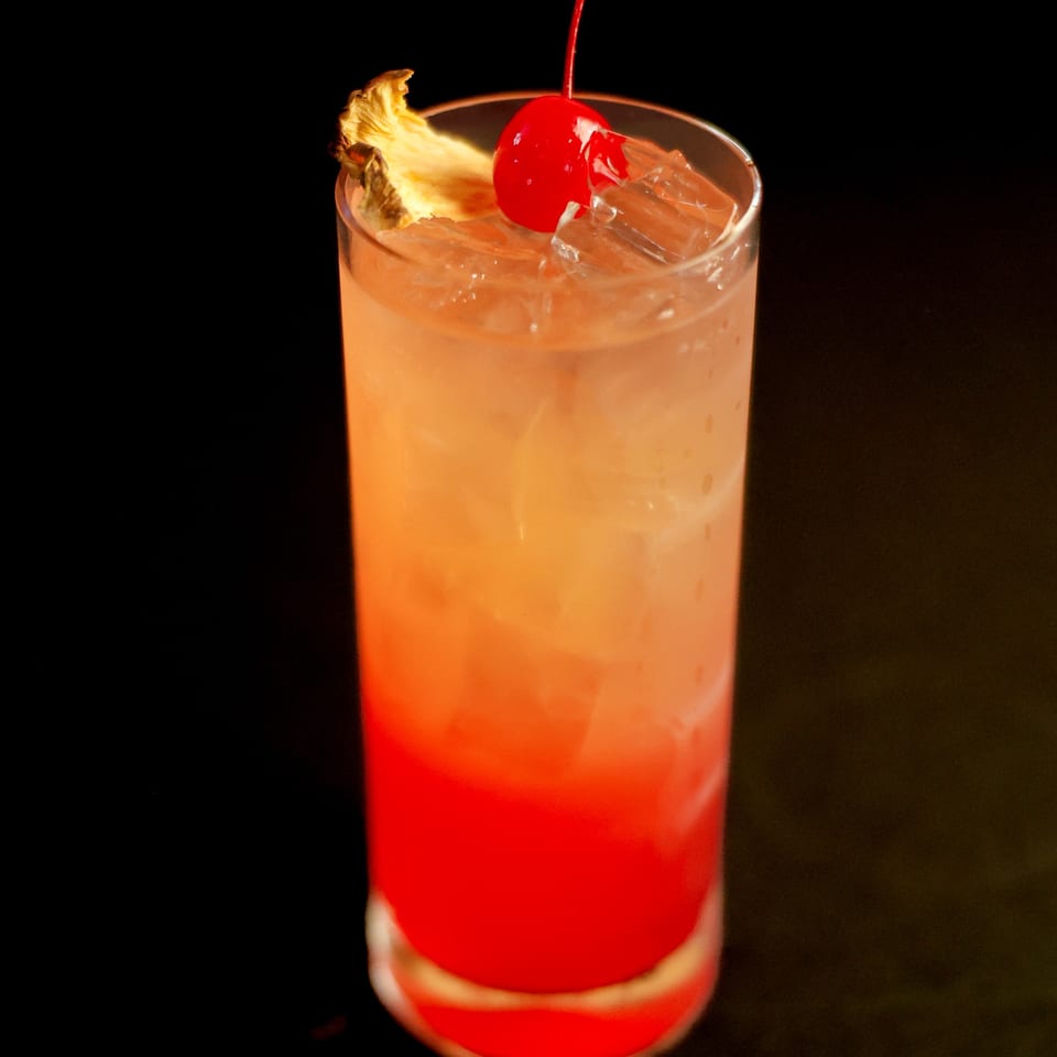 Potrillo's Mexican Grill's vibrant red and orange cocktail, garnished with a pineapple slice and cherry.