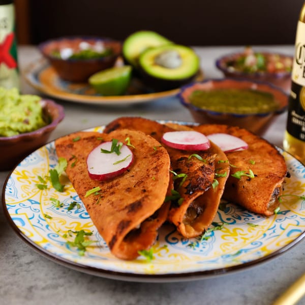 Three Potrillo's Mexican Grill tacos with radish and cilantro, with guacamole, salsa, and avocado.