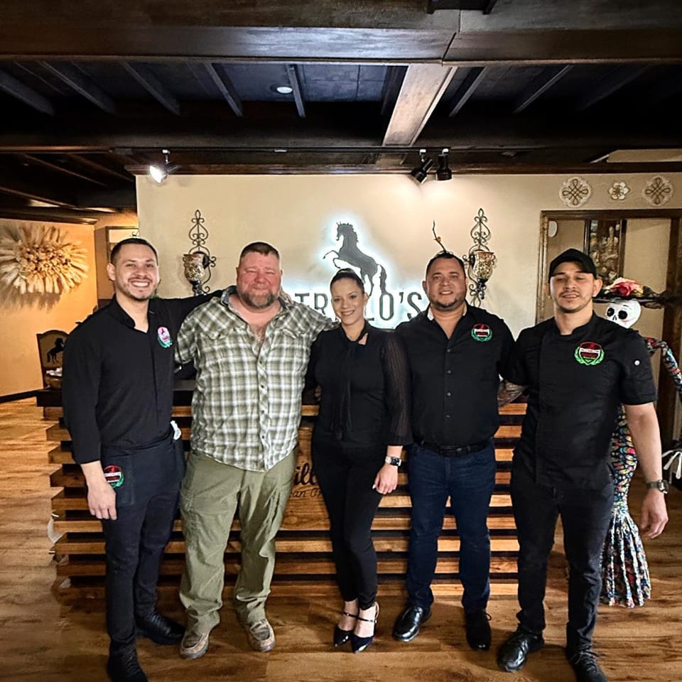 Five Potrillo's Mexican Grill staff members pose in front of the restaurant's logo.