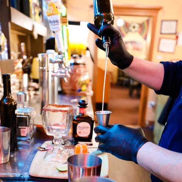 A bartender in black gloves pours a drink from a bottle into a jigger at Potrillo's Mexican Grill.