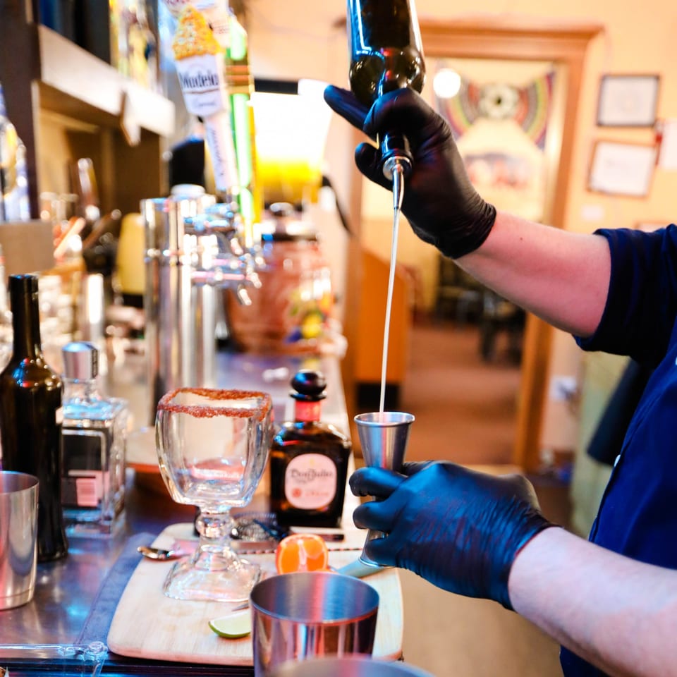 A bartender in black gloves pours a drink from a bottle into a jigger at Potrillo's Mexican Grill.