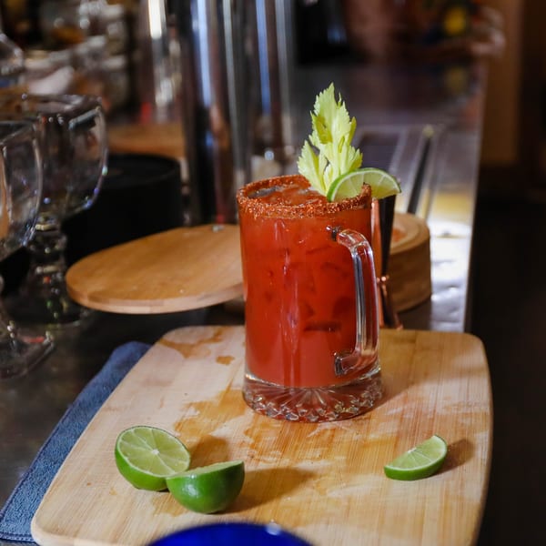 A Potrillo's Mexican Grill Michelada cocktail with a chili-lime rim, celery, and lime wedges.