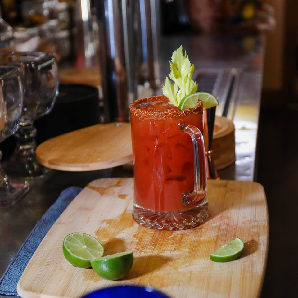 A Potrillo's Mexican Grill Michelada cocktail with a chili-lime rim, celery, and lime wedges.