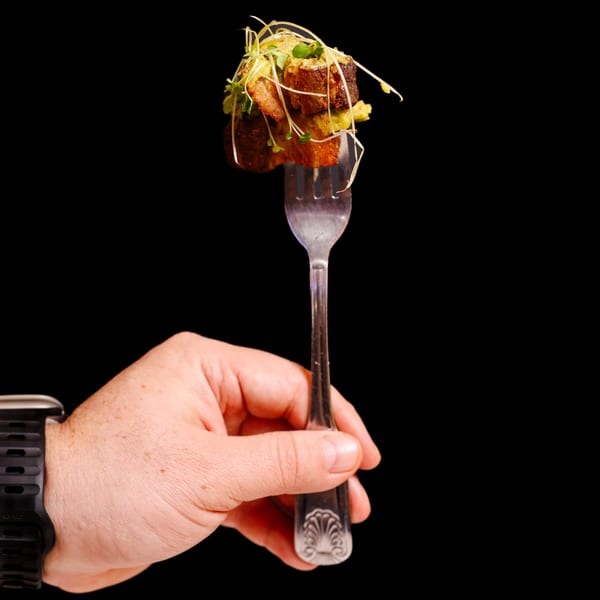 A hand holds a fork with a bite of Potrillo's Mexican Grill's food, garnished with microgreens.