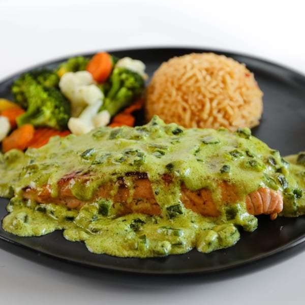 Salmon fillet with green sauce, rice, and mixed vegetables on a black plate at Potrillo's Mexican Grill.