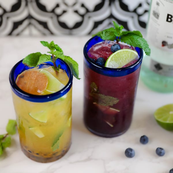 Two vibrant Potrillo's Mexican Grill cocktails, one yellow and one purple, garnished with mint and fruit.