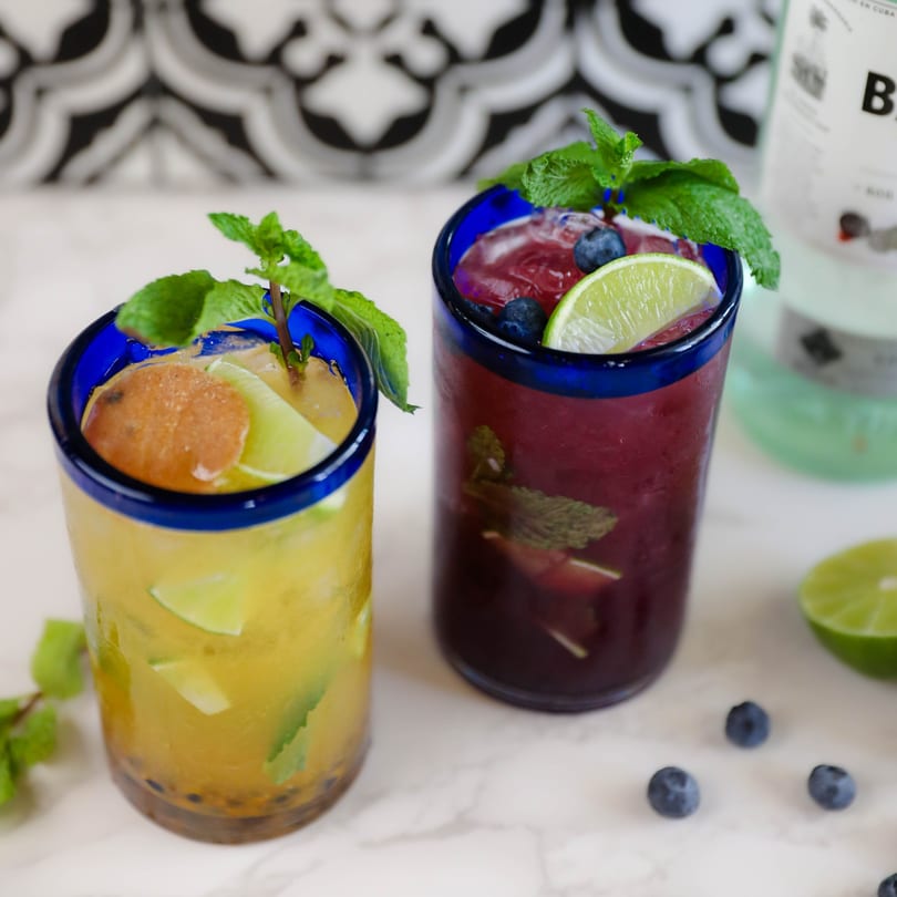 Two vibrant Potrillo's Mexican Grill cocktails, one yellow and one purple, garnished with mint and fruit.