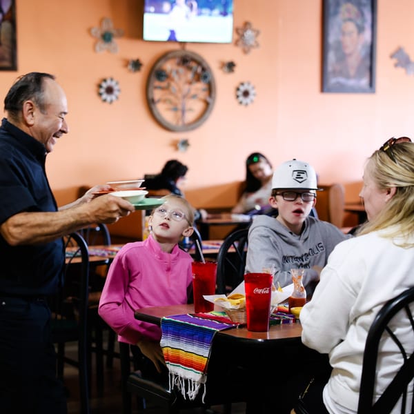 A server delivers food to a family seated at a table in Potrillo's Mexican Grill.