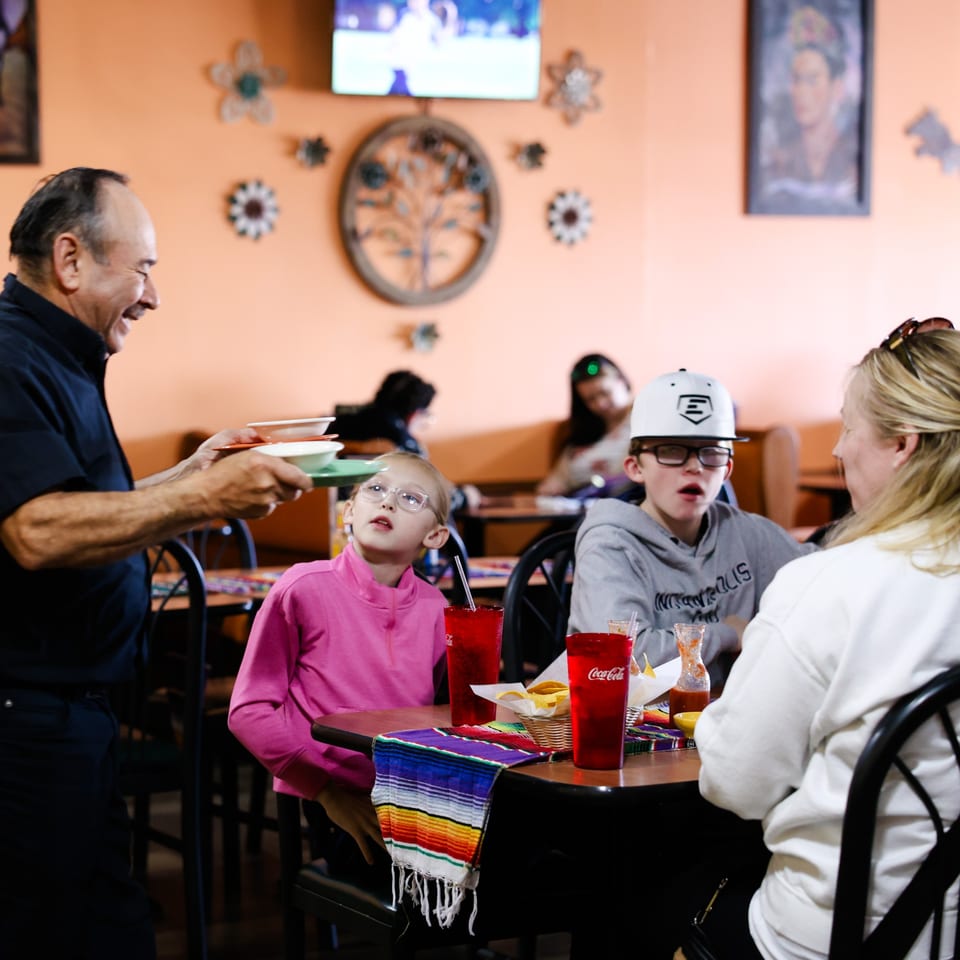 A server delivers food to a family seated at a table in Potrillo's Mexican Grill.